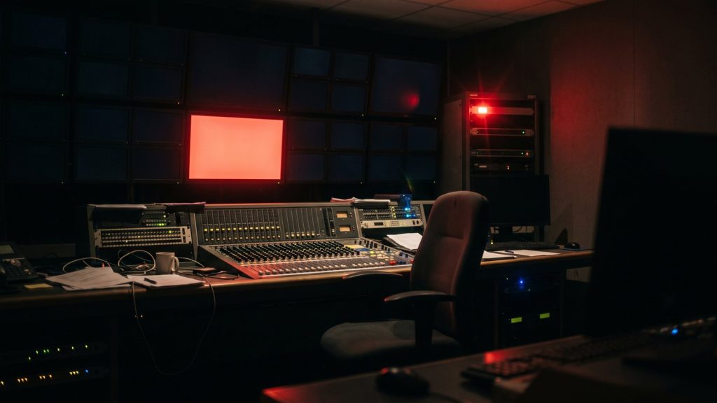 Sala de control de televisión a oscuras con una pantalla encendida en rojo y una luz de al aire