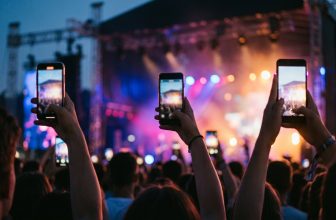 Manos de jóvenes sosteniendo teléfonos en vertical durante un concierto al atardecer