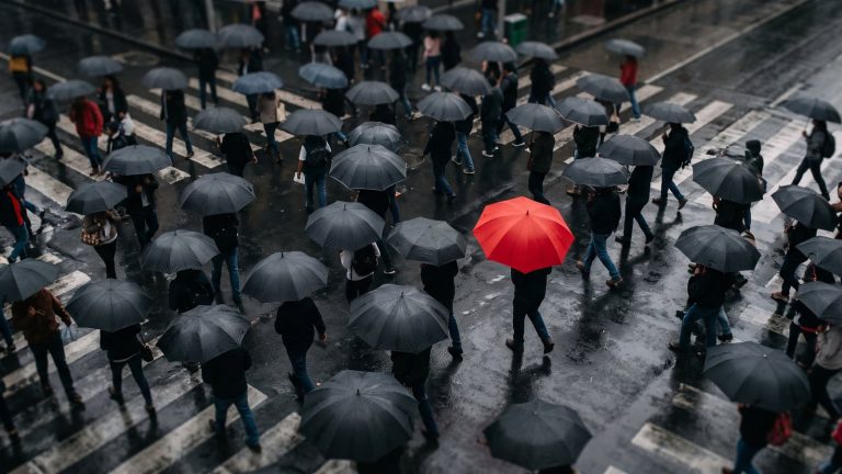Un paraguas rojo entre una multitud de paraguas negros en una calle lluviosa
