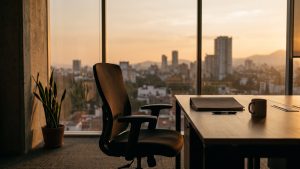 Silla de oficina vacía frente a una ventana al atardecer, con una carpeta cerrada
